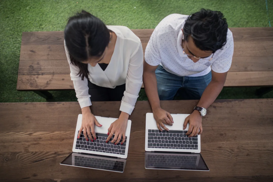 Dos personas trabajando una al lado de la otra con sus portátiles, vistas desde arriba